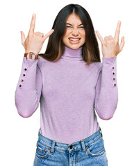 Young beautiful teen girl wearing turtleneck sweater shouting with crazy expression doing rock symbol with hands up. music star. heavy music concept.