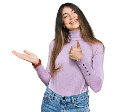 Young beautiful teen girl wearing turtleneck sweater showing palm hand and doing ok gesture with thumbs up, smiling happy and cheerful