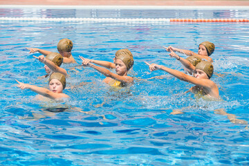 Synchronized swimmers pointing up out of the water in action. Arm movements of synchronized swimmers. Synchronized swimming team performing a synchronized routine of elaborate movements in the water.