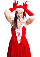 Young beautiful caucasian woman wearing santa claus costume posing funny and crazy with fingers on head as bunny ears, smiling cheerful
