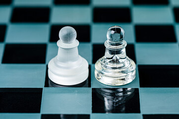 two opponent glass chess pawns on a glass chess board, black background