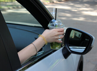 Drunk driving concept. A woman put her hand with a cocktail out of the open car window
