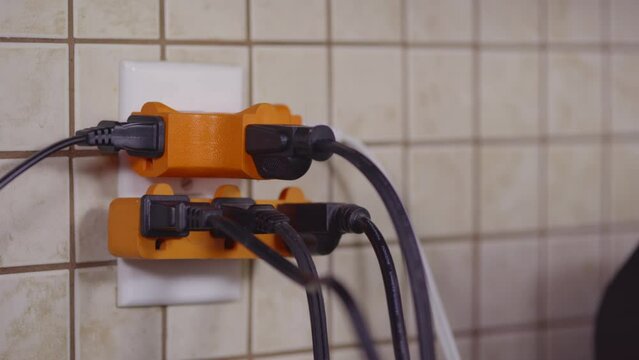 An overloaded outlet is fitted with plug splitters. A hand comes into frame and plugs one more cord into the outlet.