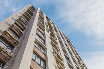 Facade of a high-rise multi-storey residential building decorated with modern materials against the sky. Modern low angle view of building