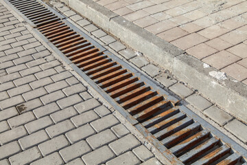 Weathering for water in a court.drainage grate of a storm system on a pedestrian sidewalk made of...