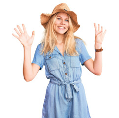 Young beautiful blonde woman wearing summer hat and dress showing and pointing up with fingers...