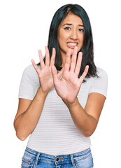 Beautiful asian young woman wearing casual white t shirt afraid and terrified with fear expression stop gesture with hands, shouting in shock. panic concept.