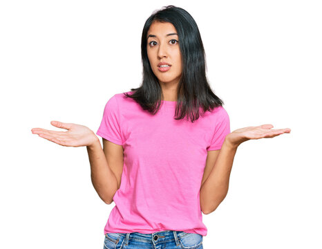Beautiful asian young woman wearing casual pink t shirt clueless and confused expression with arms and hands raised. doubt concept.