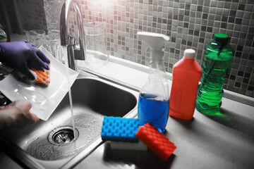 Fototapeta premium A white bottle with dishwashing gel on the background of a sink with dirty dishes and pouring water from a tap.