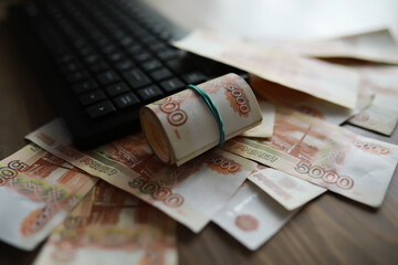 Stacks of 5000 ruble banknotes on the table next to the laptop. Savings and investments in the...