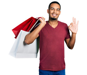 Young african american man holding shopping bags doing ok sign with fingers, smiling friendly...