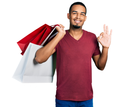 Young african american man holding shopping bags doing ok sign with fingers, smiling friendly gesturing excellent symbol - Powered by Adobe