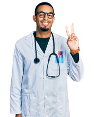 Young african american man wearing doctor uniform and stethoscope showing and pointing up with fingers number two while smiling confident and happy.