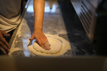 Chef kneading pizza dough with flour on kitchen table. Bakery or pizza baking concept