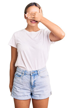 Young beautiful blonde woman wearing casual white tshirt smiling and laughing with hand on face covering eyes for surprise. blind concept.