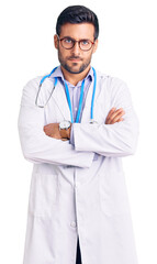 Young hispanic man wearing doctor uniform and stethoscope skeptic and nervous, disapproving...