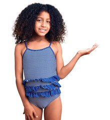 African american child with curly hair wearing swimwear smiling cheerful presenting and pointing with palm of hand looking at the camera.