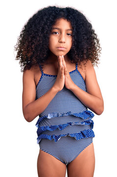 African american child with curly hair wearing swimwear praying with hands together asking for forgiveness smiling confident.