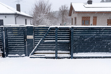 A modern gate with a letterbox and a wireless card reader, mounted in an anthracite panel fence, covered with snow.