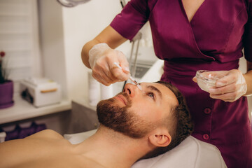 Fototapeta na wymiar Cosmetologist applying mask on man's face in spa salon, top view