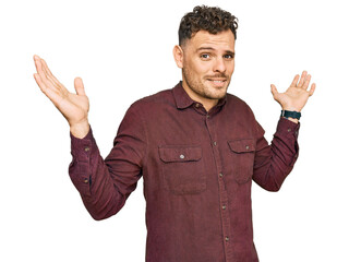 Young hispanic man wearing casual clothes clueless and confused expression with arms and hands...