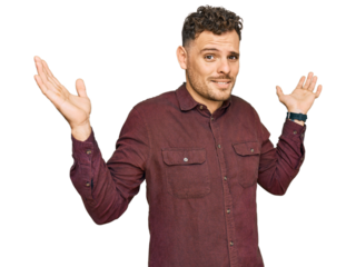 Young hispanic man wearing casual clothes clueless and confused expression with arms and hands raised. doubt concept.