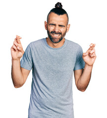 Hispanic man with ponytail wearing casual grey t shirt gesturing finger crossed smiling with hope...
