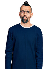 Fototapeta premium Hispanic man with ponytail wearing casual sweater and glasses making fish face with lips, crazy and comical gesture. funny expression.