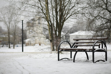 Fototapeta na wymiar park bench on a winter alley at snowfall. bench with snow after snowstorm or in snow calamity in europe