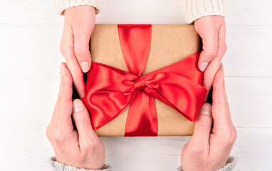 Woman's and man's hands hold a gift box with red bow. Gifts concept for the holidays. Top view....
