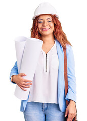 Young latin woman wearing architect hardhat and leather bag holding blueprints looking positive and happy standing and smiling with a confident smile showing teeth