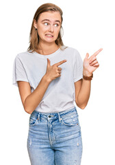 Beautiful young blonde woman wearing casual white t shirt pointing aside worried and nervous with...