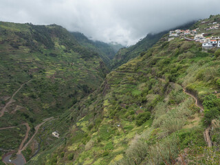 View of valley with green mountains and tropical plants, road and stream from hiking trail Levada...