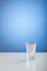 An empty frozen shot glass on a white table with light blue background