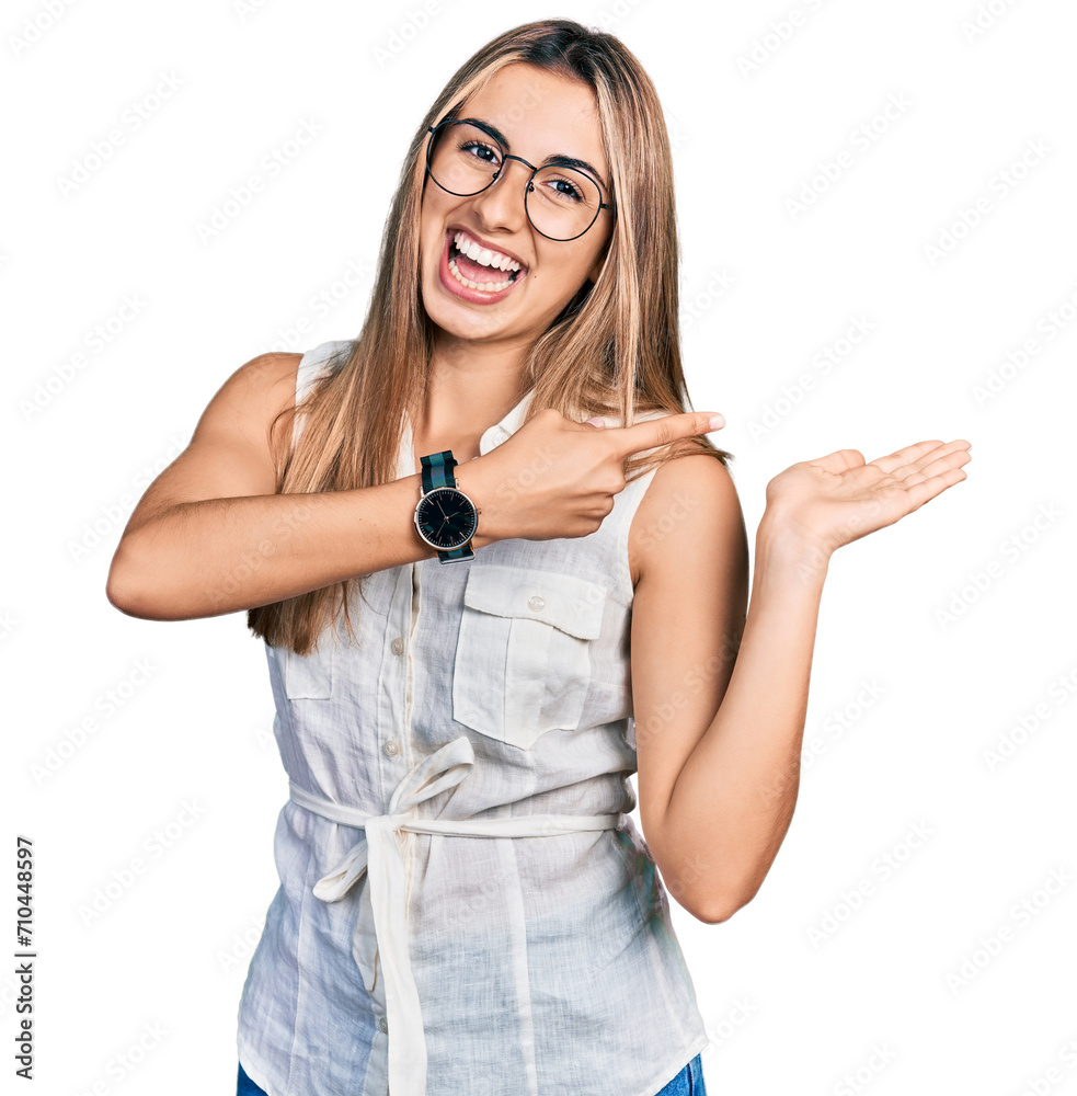 Sticker Hispanic young woman wearing casual white shirt amazed and smiling to the camera while presenting with hand and pointing with finger.