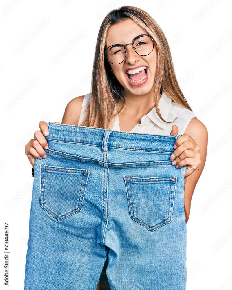 Canvas Prints hispanic young woman holding slim jeans winking looking at the camera with sexy expression, cheerful