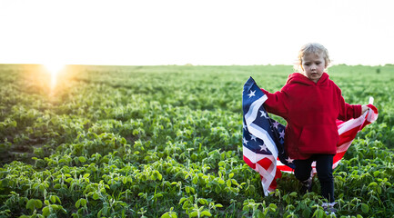 flag of America on shoulders of a child. girl in the background of sunset. Little American...