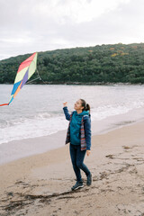 Smiling girl walking along the seashore with a colorful kite on a string