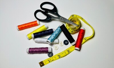 spools of thread, scissors, buttons and measuring tape on white background