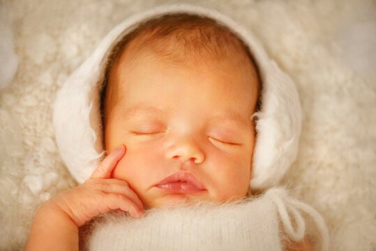 Newborn baby sleeps sweetly. Portrait of a girl. The baby is sleeping. Baby girl in fur headphones. The small hand of a newborn child touched his cheek. Newborn photo session. Winter. Christmas
