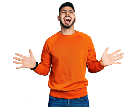 Young hispanic man with beard wearing casual orange sweater crazy and mad shouting and yelling with aggressive expression and arms raised. frustration concept.