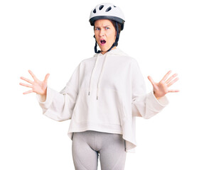 Beautiful brunette young woman wearing bike helmet and sporty clothes crazy and mad shouting and yelling with aggressive expression and arms raised. frustration concept.