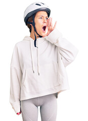 Beautiful brunette young woman wearing bike helmet and sporty clothes shouting and screaming loud to side with hand on mouth. communication concept.