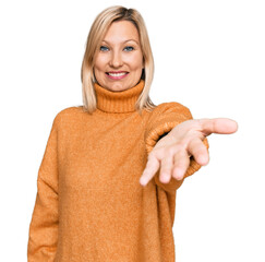 Middle age caucasian woman wearing casual winter sweater smiling cheerful offering palm hand giving assistance and acceptance.
