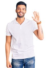 Young handsome hispanic man wearing casual clothes waiving saying hello happy and smiling, friendly welcome gesture
