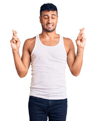 Young hispanic man wearing casual clothes gesturing finger crossed smiling with hope and eyes closed. luck and superstitious concept.