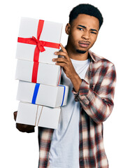 Young african american man holding gifts skeptic and nervous, frowning upset because of problem....