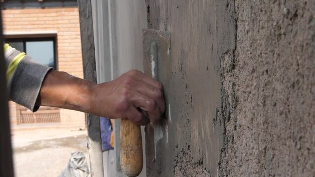 Construction worker plastering wall using concrete. Latino man placing cement on wall. Close up of man plastering wall with concrete.