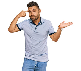 Handsome man with beard wearing casual clothes confused and annoyed with open palm showing copy space and pointing finger to forehead. think about it.