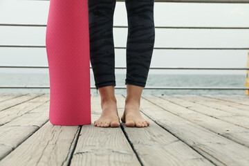 Female feet and pink yoga mat on wooden floor outdoors, close up